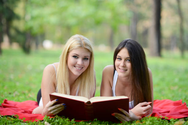 istock Two girls reading book in park 661515194