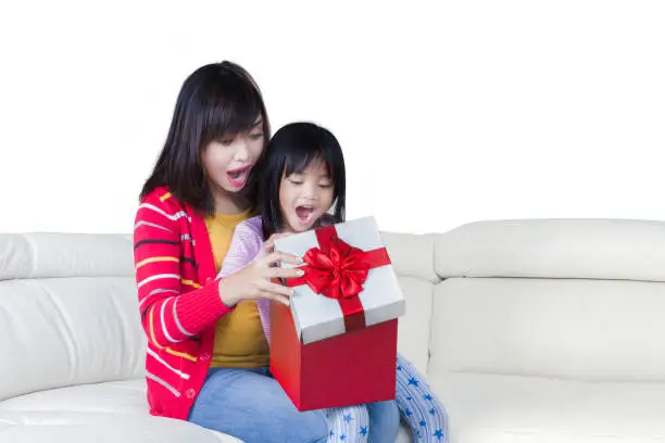Portrait of mother and cute child showing surprised expression while opening gift box together, isolated on white background