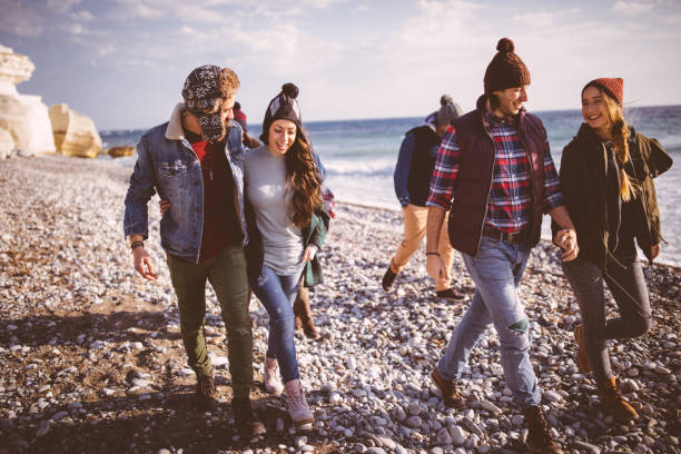 gruppo di giovani amici che camminano lungo la spiaggia in inverno - fun knit hat adult dating foto e immagini stock