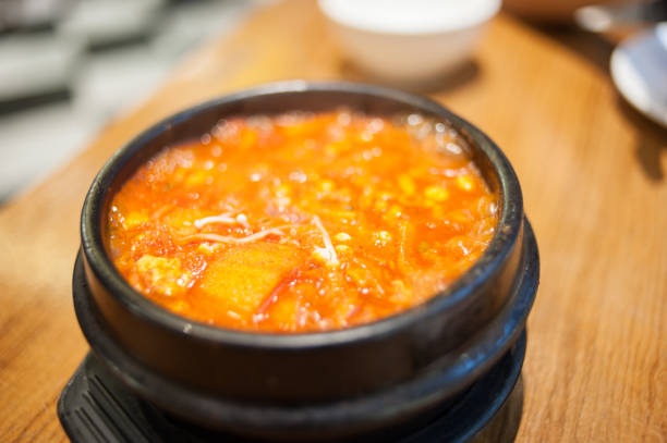 Korean food (Kimchi Jjigae), Kimchi soup with tofu, pork, scallion and chili in Korean stone bowl on black background