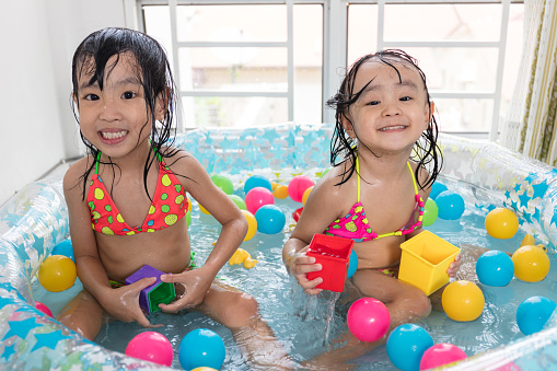 Happy Asian Chinese little sisters playing in the inflatable pool inside the house.