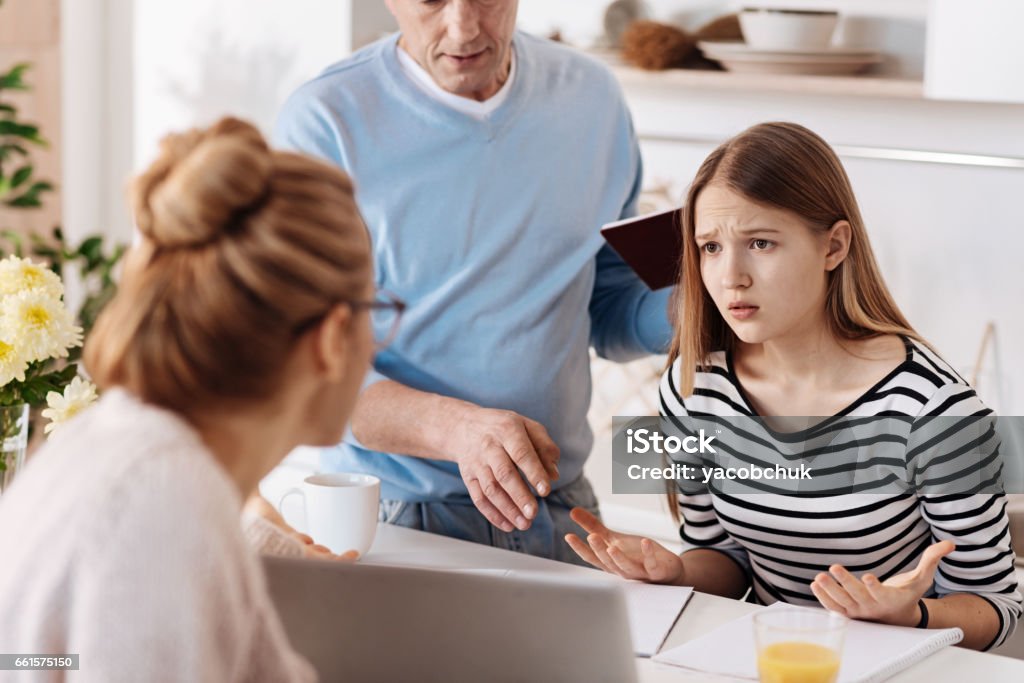 Sad girl doing homework with her parents I do not understand it. Depressed pleasant girl sitting at the table and doing homework while her parents assisting her Teenager Stock Photo