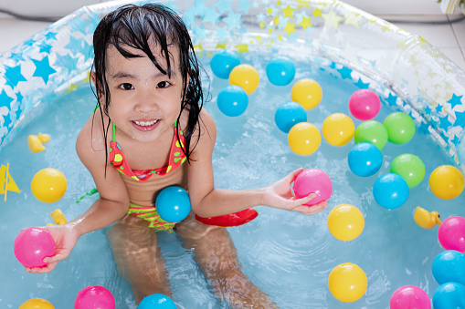 Happy Asian Chinese little girl playing in the inflatable pool inside the house.