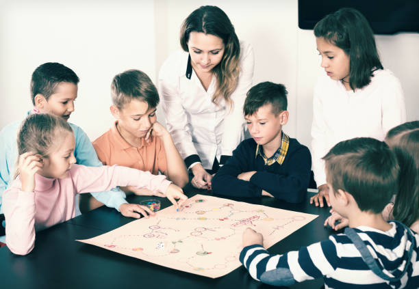 istock Teacher and happy kids sitting  at table with board game 661580494