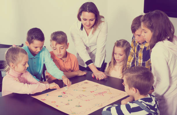 istock Children sitting at table with board game and dice in school 661580528