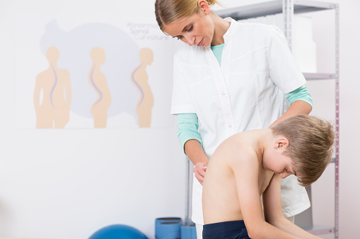 Doctor and boy with scoliosis during rehabilitation in hospital