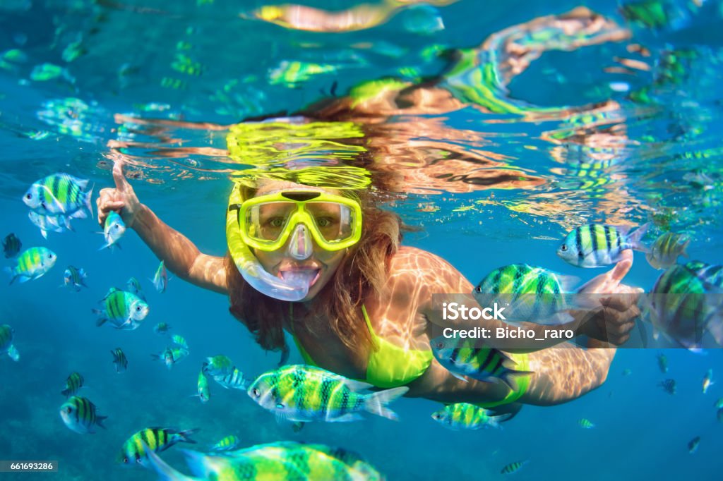 Girl in snorkeling mask dive underwater with coral reef fishes Happy family - girl in snorkeling mask dive underwater with fishes school in coral reef sea pool. Travel lifestyle, water sport outdoor adventure, swimming lessons on summer beach holidays with child. Snorkeling Stock Photo
