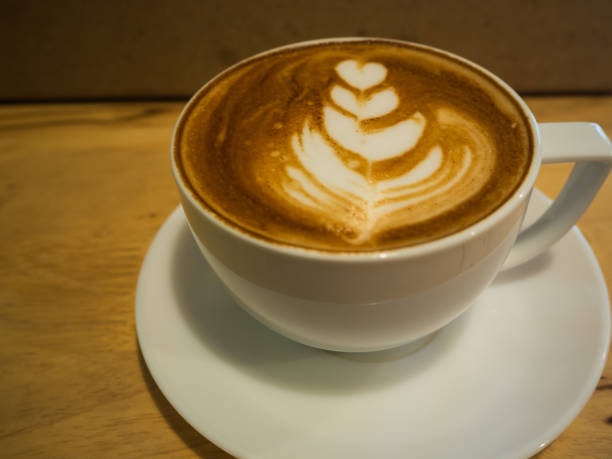 uma xícara de café com padrão de coração em uma xícara branca na mesa de madeira - lattã© - fotografias e filmes do acervo