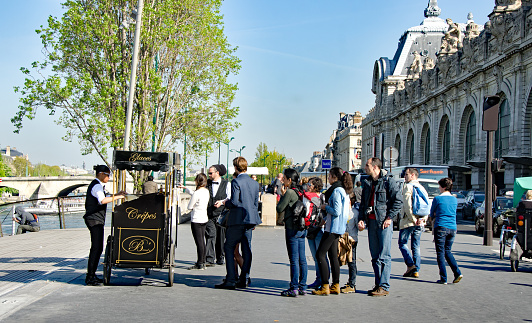 Paris street scene showing flower and market shops. This area is known for tourism as it is near the Louve and other museums. The people are both tourists and residents.