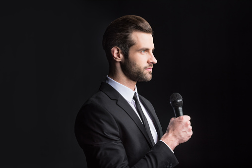 Young handsome man holding microphone and looking at distance on black