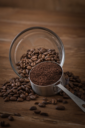 Combination of both ground coffee and whole bean coffee in a scoop and small measuring bowl respectively