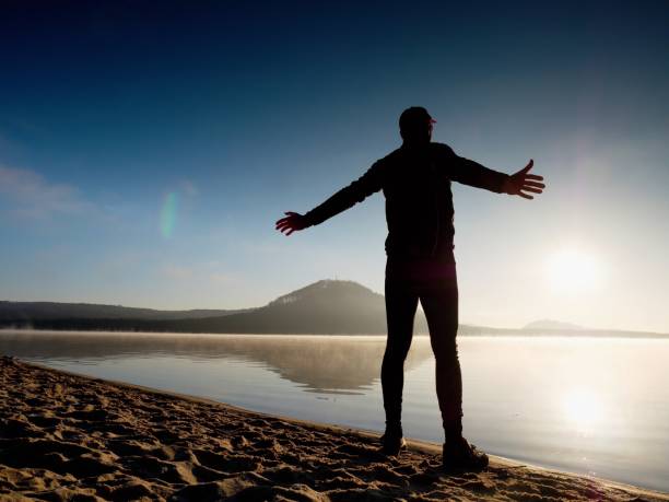 istock Man exercising on beach.  Silhouette of active man exercising  and stretching at lake 661798122