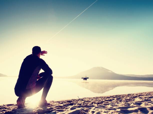 istock Man exercising on beach.  Silhouette of active man exercising  and stretching at lake 661799552