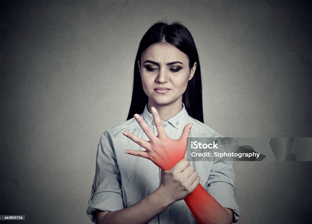 Woman holding her painful wrist Woman holding her painful wrist colored in red isolated on gray wall background. Adult Stock Photo