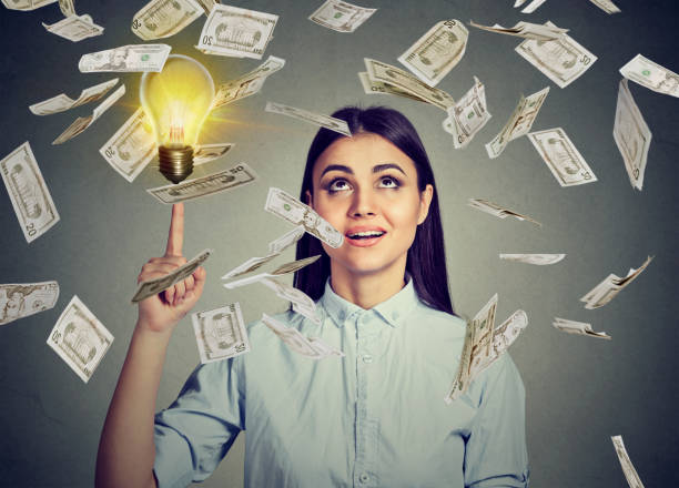 istock Woman under money rain pointing up at a bright idea light bulb 661806044