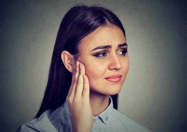 Tinnitus. Closeup portrait sick female having ear pain touching her painful head Tinnitus. Closeup portrait sick female having ear pain touching her painful head isolated on gray wall background neuralgia stock pictures, royalty-free photos & images