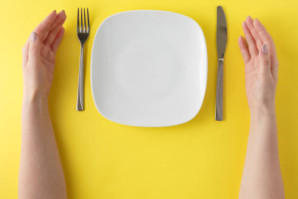 istock Closeup white ceramic dish with stainless fork and knife and woman hand on plain yelow background in top view 661832828