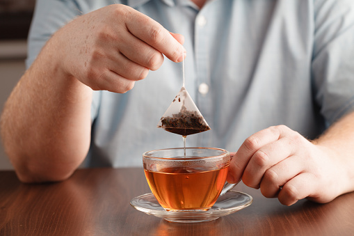 Teabag in the cup with hot water in hands