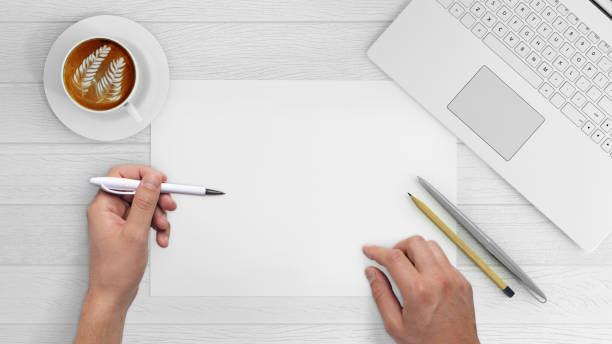 Knolling hands writing on a blank paper Direct view at hands writing on a blank paper . Office desk with laptop, coffee, notebook, pencils, and a plant. vintage wood white desk. copy space. hipster template left handed stock pictures, royalty-free photos & images