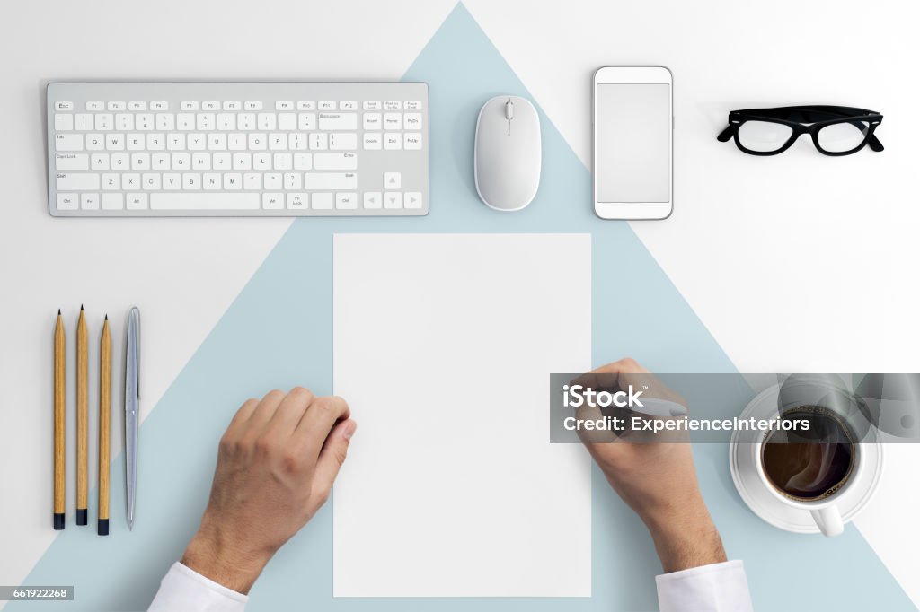 Knolling hands writing on a blank paper Direct view at hands writing on a blank paper .Office desk with pc keyboard, smartphone, coffee, notebook, pencils, white and blue desk pattern. copy space. hipster template Desk Stock Photo