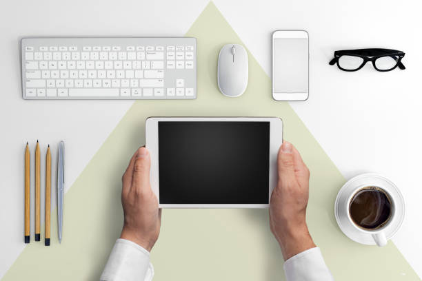 Close up of man hands holding and using a digital tablet. Business office desk background, with a PC in the back. white and green
