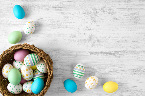 Colorful easter eggs in wicker on white rustic background.