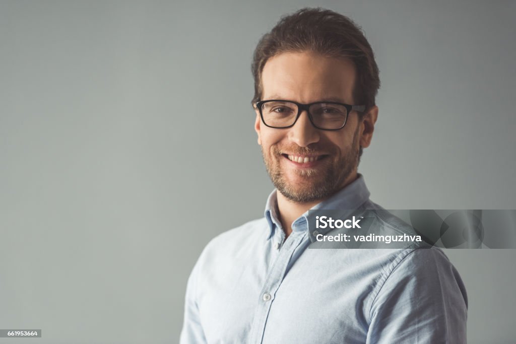 Handsome confident businessman Handsome businessman in eyeglasses is looking at camera and smiling, on gray background Adult Stock Photo