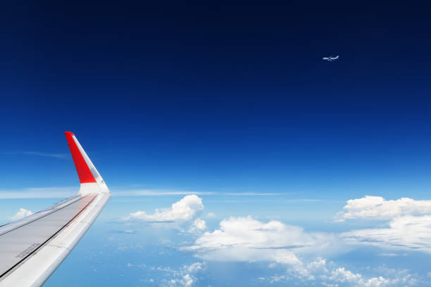 Oncoming flight traffic in mid air. Aircraft flying above beautiful earth, clouds. Aerial view of clear blue sky, aircraft wing from cabin through plane window. Travel tour background with copy space