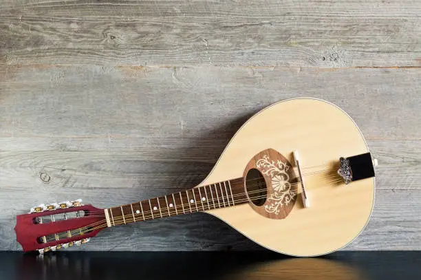 Front view of a reclined wooden flatback mandolin on a black table with a weathered wood background