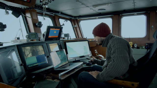 Captain of Commercial Fishing Ship Surrounded by Monitors and Screens Working with Sea Maps in his Cabin.