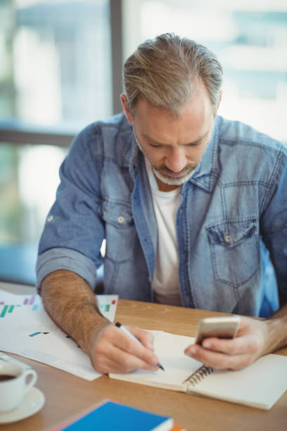 istock Male business executive writing in organizer while using mobile phone 662132604