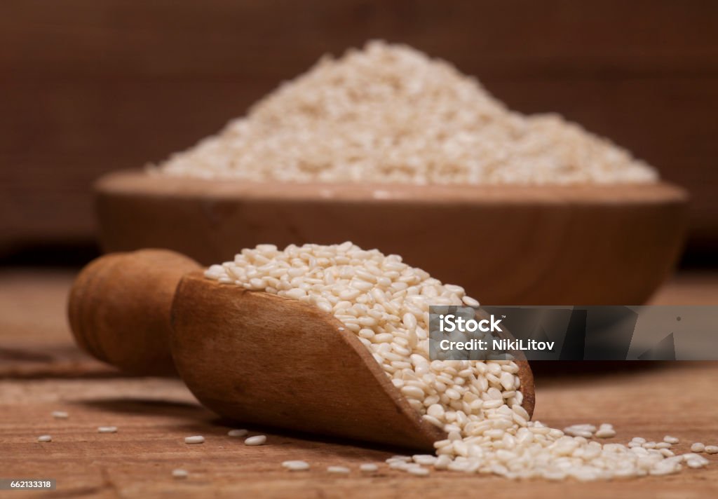 Fresh sesame seeds in a wooden bowl and spoon Fresh sesame seeds in a wooden bowl and spoon on wooden background Agriculture Stock Photo