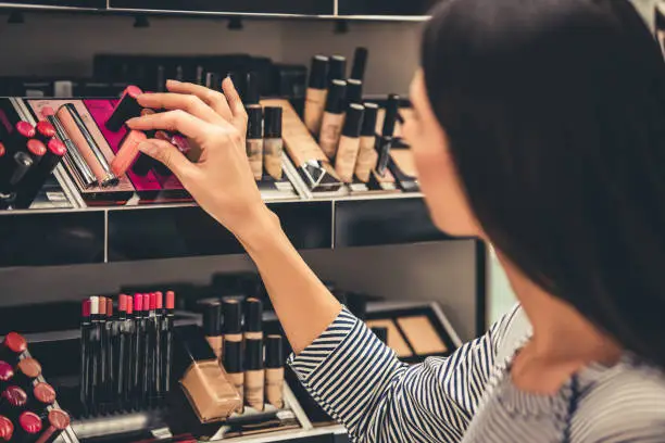 Beautiful girl is choosing lipstick while doing shopping in the mall