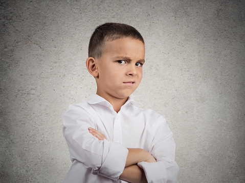 Closeup up portrait headshot suspicious, cautious child boy looking at you with disbelief, skepticism isolated grey wall background. Human facial expressions emotions body language perception attitude