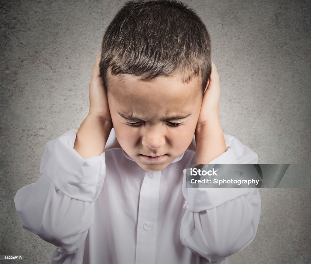 Closeup portrait, headshot child, boy covering ears with hands Closeup portrait, headshot child, boy covering ears with hands, doesn't want to hear loud noise, conversation isolated grey wall background. Human face expression, emotion, feeling reaction perception Confrontation Stock Photo