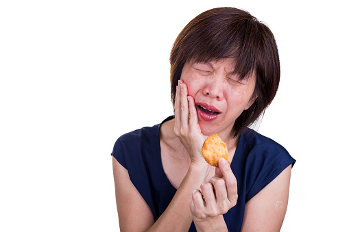 Asian women with intense toothache pain after biting cookie, on white background