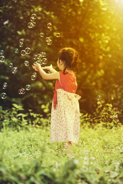 istock Asian girl catches soap bubbles on nature background. Back view. 662468710