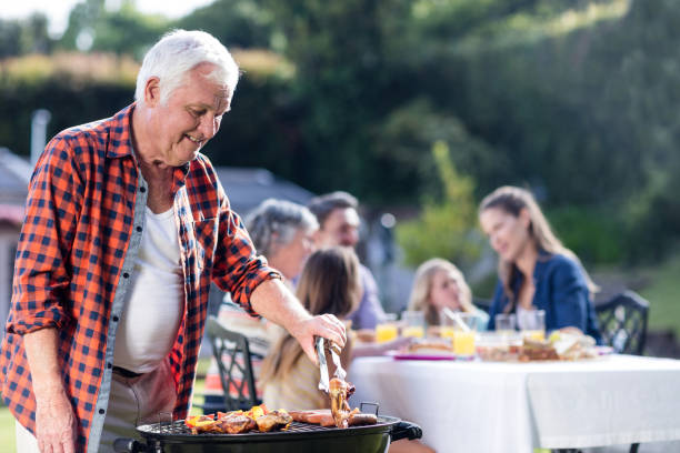istock Senior man at barbecue grill while family having lunch in background 662475558