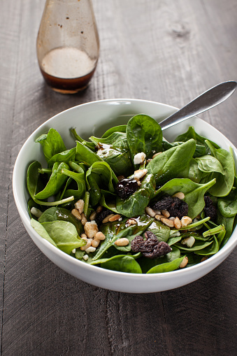 Balsamic Spinach Salad with dried cherries, roasted pine nuts, Feta cheese, and a homemade balsamic vinaigrette on a dark wooden background with a glass flask of dressing