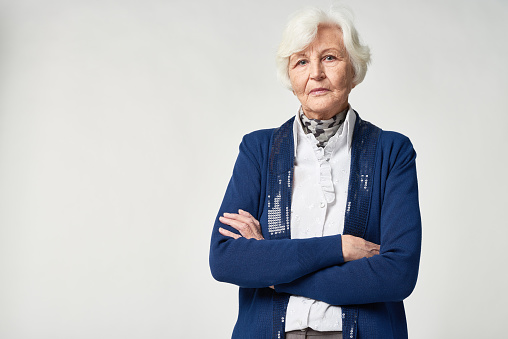 Serious senior woman in fashionable clothes crossing arms on chest and looking at camera in studio