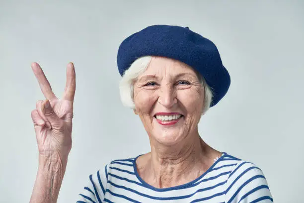 Cheerful senior French woman showing two fingers as symbol of greeting