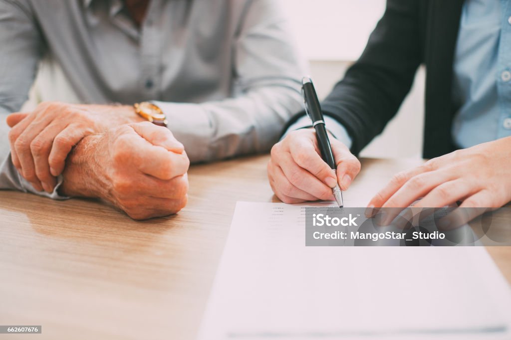 Unrecognizable woman signing contract at meeting_tone Unrecognizable woman signing contract at meeting, businessman sitting near her and controlling process of deal. Or female hands analyzing or examining document. Paperwork or partnership concept Senior Adult Stock Photo