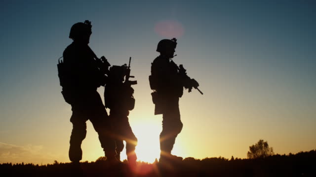 Squad of Three Fully Equipped and Armed Soldiers Standing in Desert Environment in Sunset Light. Slow Motion.