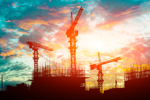 Tower crane and high-rise buildings silhouettes under construction at construction site at yellow sky sunset. Orange yellow sky. Shooting the building new houses in the city