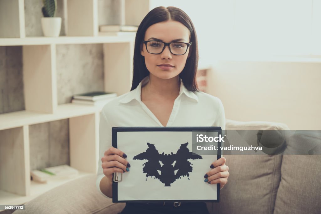 Beautiful young psychologist Beautiful female psychologist is showing the Ink blot test and looking at camera while sitting in her office Mental Health Professional Stock Photo