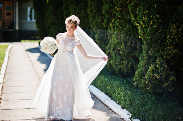 istock Awesome gorgeous blonde bride with wedding bouquet at hands at sunny day. 662904564