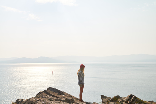 Female traveler in hat walking on rocks, seascape