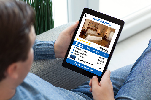 man in jeans holding tablet computer with app hotel booking on screen