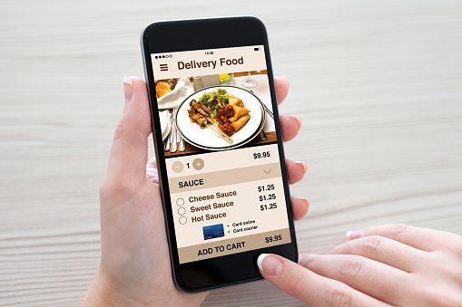 Women hands holding phone with app delivery food on screen over table