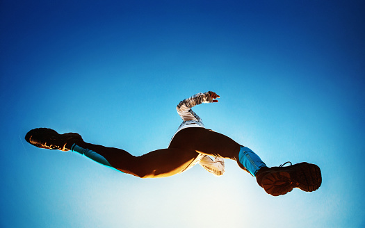 Low angle view of uneecognizable man running in the morning. He's jumping dirextly over camera, shot with wide angle lens. Intense blue sky in the background